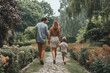 © bajita111122 - A young family is walking hand in hand along a lush, sunlit park path, exuding happiness and tranquility..