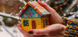 Hands cupping a miniature house painted in vibrant colors, illustrating the joy and personality of home even in the bleakness of winter