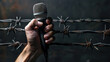hand holds a microphone, against the background of rusty barbed wire and a dark wall, free space for text, banner
