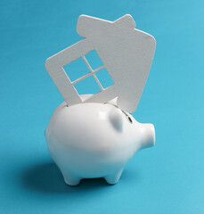 Wall Mural - Piggy bank with a house model on blue background