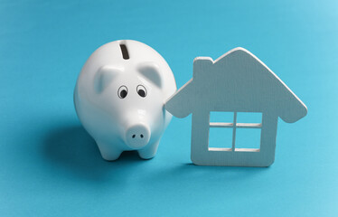 Wall Mural - Piggy bank with a house model on blue background