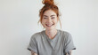 A cheerful woman with red hair tied in a bun, laughing joyfully in a casual grey t-shirt, her freckles and bright expression conveying happiness.