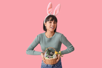 Canvas Print - Pretty young woman in bunny ears holding wicker Easter basket with cosmetics on pink background