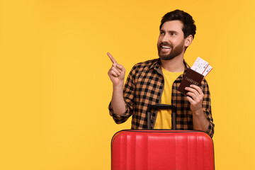 Wall Mural - Smiling man with passport, tickets and suitcase pointing at something on yellow background. Space for text