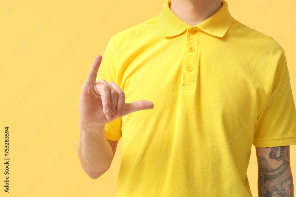 Young deaf mute man using sign language on yellow background