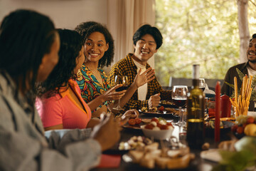 Wall Mural - Happy friends enjoying in conversation and drinking wine during festive dinner at home party