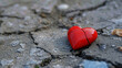 A red stone heart smashed in a cracked concrete ground, symbol for a broken heart 