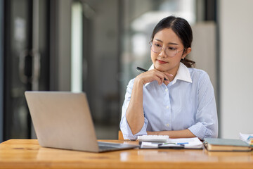 Wall Mural - Asian Businesswoman Using laptop computer and working at office with calculator document on desk, doing planning analyzing the financial report, business plan investment, finance analysis concept.
