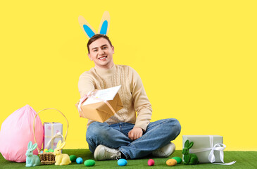 Poster - Happy young man in bunny ears with gift boxes and Easter eggs celebrating on yellow background