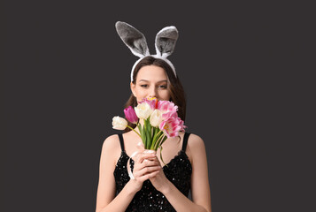 Young woman in Easter bunny ears headband with bouquet of tulips on black background