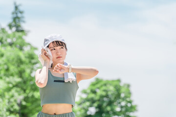 Wall Mural - 公園でジョギング・ランニング中に汗を拭く女性（暑い・気温・温度・不満・不快・ベトベト・湿度）
