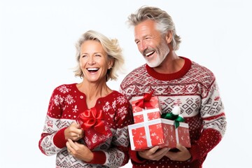 An elderly couple wearing Christmas sweaters, holding gift-wrapped presents and smiling