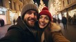 A happy couple smiling and taking a selfie in front of a festive city street at night.
