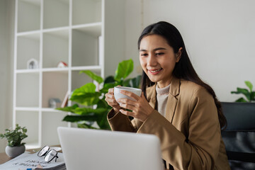 smiling businesswoman drinking coffee and working on laptop in green modern office. Nice Environment Office. Eco-Friendly Concept