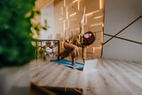 Fototapeta Tęcza - Woman practicing Warrior yoga pose at office using online lesson standing on a mat