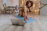 Fototapeta Tęcza - Woman practicing yoga at office using online lesson standing on a mat
