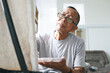 © Queenmoonlite Studio - Senior Asian man wear glasses, sit and painting picture inside of the house. Happy retirement lifestyle concept.