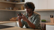 © Yuliia - Moving shot carefree happy Indian man browsing smartphone laugh Arabian male smiling scrolling social media network app looking at mobile phone laughing smile enjoy funny video online at home kitchen
