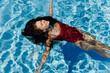 © SHOTPRIME STUDIO - Happy woman swimming in pool in red swimsuit with loose long hair relaxed with hands up in sunlight, skin protection with sunscreen, concept of relaxing on vacation in tropical climate.