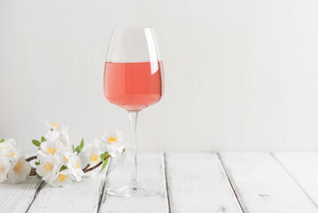 Wall Mural - A glass of rose wine with a decorative flowering cherry branch on a white wooden table. Side view, selective focus. Pink wine.