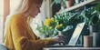A young woman in a fashionable sweater works at a laptop against the background of indoor plants