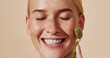© Artem Varnitsin - Close up highly detailed shot of a smiling woman using a face roller. Female with closed eyes and freckled skin using jade roller over pastel backdrop.