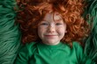 Ginger haired child with curly hair and freckles smiles in green background