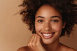 A woman with curly hair is smiling, wearing a white shirt and is looking directly at the camera. Woman smiling while touching her flawless glowy skin with copy space for your advertisement, skincare