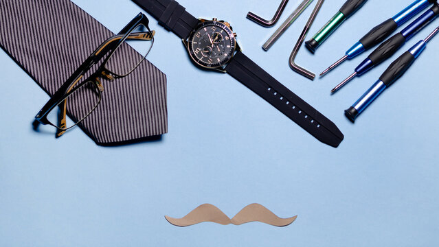 several tools, a tie and a paper mustache on a light blue background. The image conveys a fun and humorous atmosphere. father's day concept.copyspace