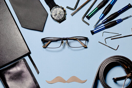 several tools, a tie and a paper mustache on a light blue background. The image conveys a fun and humorous atmosphere. father's day concept. copyspace