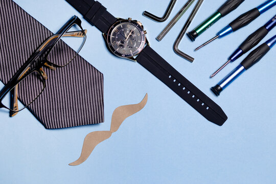 several tools, a tie and a paper mustache on a light blue background. The image conveys a fun and humorous atmosphere. father's day concept. copyspace