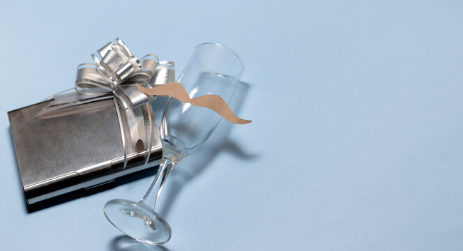 a glass cup with a mustache and on the side a gift in a gray and shiny box. Father's day. copyspace