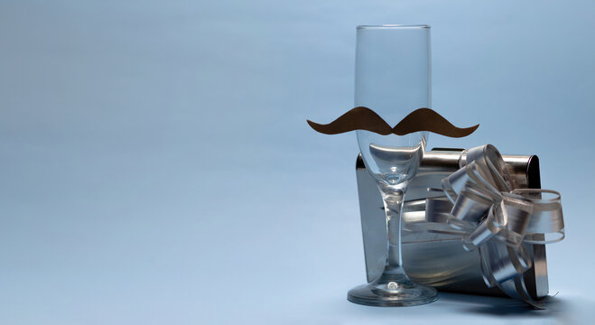 a glass cup with a mustache and on the side a gift in a gray and shiny box. Father's day. copyspace