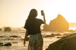 © Luis Herrera/Stocksy - woman capturing sunset on the beach with her phone