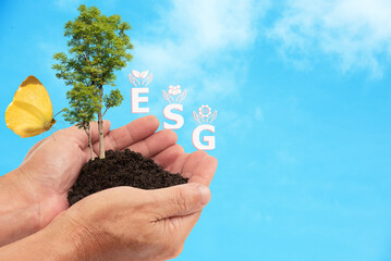 In his hand was soil for planting tree ,wind turbine ,ESG letters and icons on nature background.Investment concept.