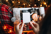 Female Hands Holding A Blank White Postcard Near Christmas Tree