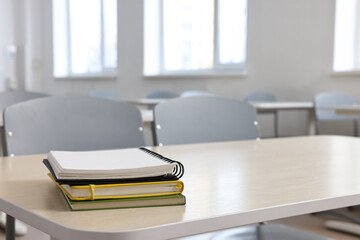 Wall Mural - Stack of notebooks on wooden desk in empty classroom. Space for text