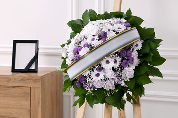 Wall Mural - Wreath of violet and white flowers, photo frame with black ribbon in room. Funeral attributes