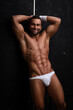 © Serge Lee - Male fitness model in white underwear on a black background. Muscular naked guy smiling in the studio. A handsome man in white shorts and with a bandage on his arm. The owner of six-pack abs