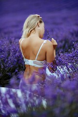 Canvas Print - A middle-aged woman sits in a lavender field and enjoys aromatherapy. Aromatherapy concept, lavender oil, photo session in lavender