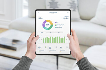 Hands hold tablet with app monitoring electricity consumption in house. Concept of energy management, technology, and smart living solutions