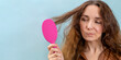 Woman holding pink hair brush, combing hair with intrigued face expression. Banner with copy space.