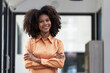 © Songsak C - Happy African American young woman standing with arms crossed in an office.