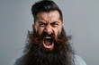 Close up portrait of angry mad young man with long beard shouting isolated on light grey background
