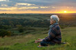 Elderly woman meditating on a hill at sunset in summer