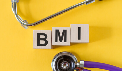 Wall Mural - The word BMI is written on wooden cubes near a stethoscope on a yellow background. BMI - body mass index. Medical concept.