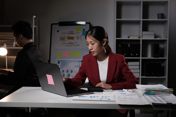 Wall Mural - A woman in a red jacket is sitting at a desk with a laptop open