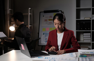 Poster - A woman in a red jacket is sitting at a desk with a laptop and a calculator