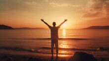 A Man Stands On The Beach, Arms Raised In The Air, With The Sun Setting In The Background. Concept Of Freedom And Joy, As The Man Is Celebrating Or Expressing His Happiness