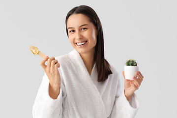 Canvas Print - Beautiful young happy woman in bathrobe holding spatula with sugaring paste and cactus on grey background